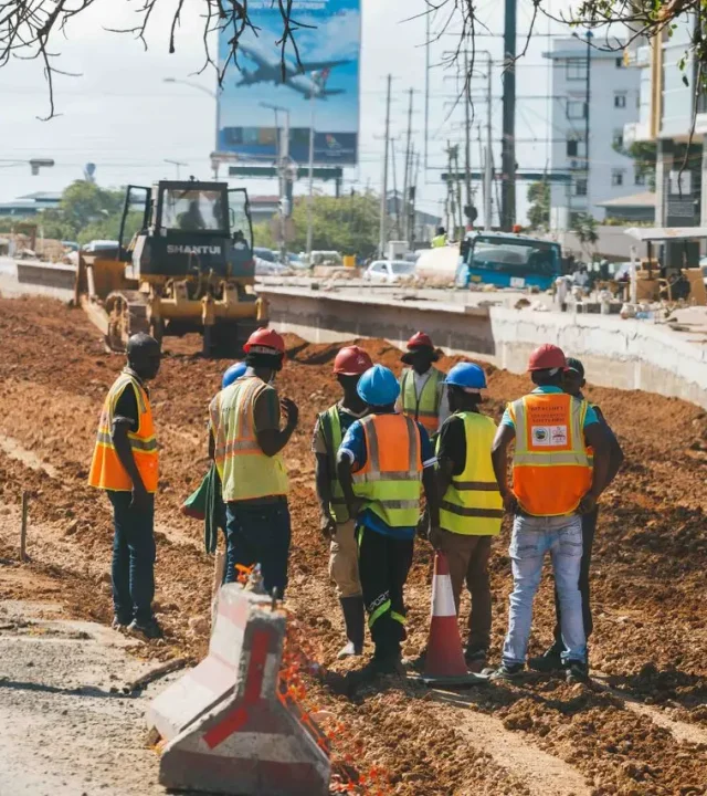 Construction workers wearing safety gear at a busy roadwork site during the day.